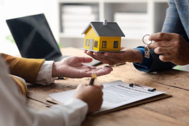 Bir ev kiralama şirketi çalışanı kira sözleşmesi imzalamayı kabul eden bir müşteriye kira sözleşmesinin detaylarını ve şartlarını açıklayan ev anahtarlarını teslim ediyor. Ev ve gayrimenkul kiralama fikirleri.