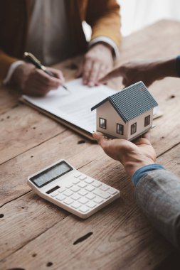 A home rental company employee is handing the house keys to a customer who has agreed to sign a rental contract, explaining the details and terms of the rental. Home and real estate rental ideas.