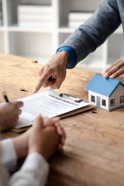 A home rental company employee is handing the house keys to a customer who has agreed to sign a rental contract, explaining the details and terms of the rental. Home and real estate rental ideas.