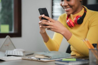 Genç bir Amerikalı kadın yeni başlayan bir iş kadınıdır, ofiste oturur ve cep telefonu kullanır, işlerini genç bir nesilden yönetir ve yönetir. Girişim işletme yönetimi kavramı.