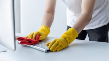 Person cleaning room, cleaning worker is using cloth to wipe computer keyboard in company office room. Cleaning staff. Concept of cleanliness in the organization.
