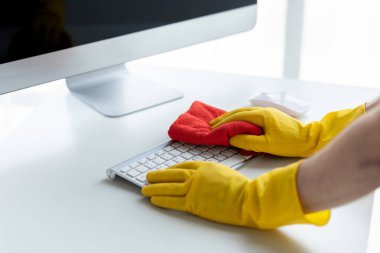 Person cleaning room, cleaning worker is using cloth to wipe computer keyboard in company office room. Cleaning staff. Concept of cleanliness in the organization.