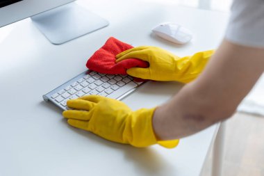 Person cleaning room, cleaning worker is using cloth to wipe computer keyboard in company office room. Cleaning staff. Concept of cleanliness in the organization.