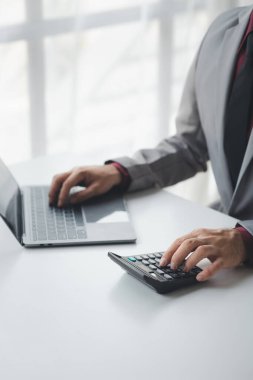 Şirketin mali belgelerindeki rakamları hesaplamak için hesap makinesi kullanan bir işadamı, şirketin nasıl büyüyeceğini planlamak için tarihsel finansal verileri analiz ediyor. Mali konsept.