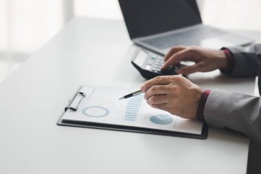 Şirketin mali belgelerindeki rakamları hesaplamak için hesap makinesi kullanan bir işadamı, şirketin nasıl büyüyeceğini planlamak için tarihsel finansal verileri analiz ediyor. Mali konsept.