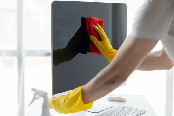 Person cleaning room, cleaning worker is using cloth to wipe computer screen in company office room. Cleaning staff. Concept of cleanliness in the organization.