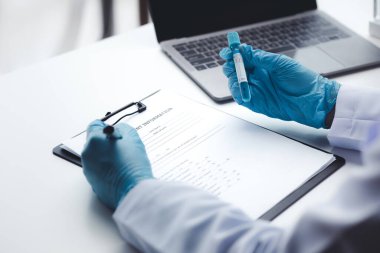 Lab assistant, a medical scientist, a chemistry researcher holds a glass tube through the blood sample, does a chemical experiment and examines a patient's blood sample. Medicine and research concept.