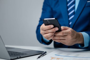 Business man looking at financial information from a mobile phone, he is checking company financial documents, he is an executive of a startup company. Concept of financial management.