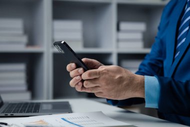 Business man looking at financial information from a mobile phone, he is checking company financial documents, he is an executive of a startup company. Concept of financial management.