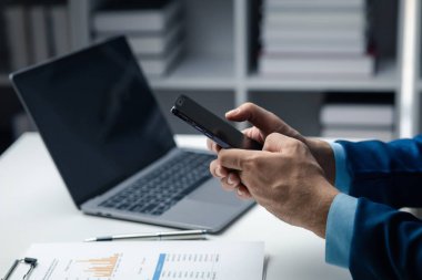 Business man looking at financial information from a mobile phone, he is checking company financial documents, he is an executive of a startup company. Concept of financial management.