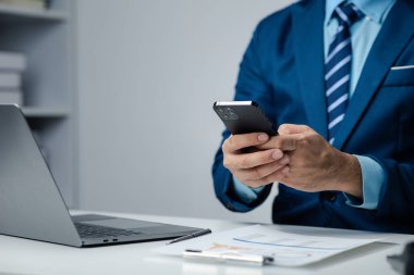 Business man looking at financial information from a mobile phone, he is checking company financial documents, he is an executive of a startup company. Concept of financial management.