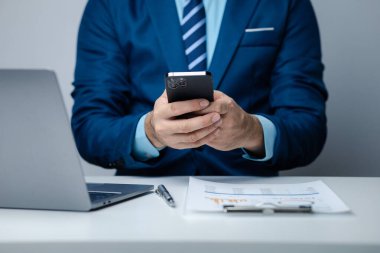 Business man looking at financial information from a mobile phone, he is checking company financial documents, he is an executive of a startup company. Concept of financial management.