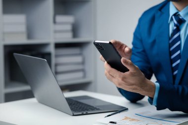 Business man looking at financial information from a mobile phone, he is checking company financial documents, he is an executive of a startup company. Concept of financial management.
