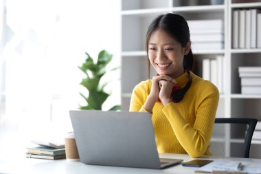 Beyaz odada dizüstü bilgisayarla oturan genç bir kadın, evde dizüstü bilgisayarla çalışan bir öğrenci, online olarak okuyan bir üniversite öğrencisi, online web eğitimi kavramı.