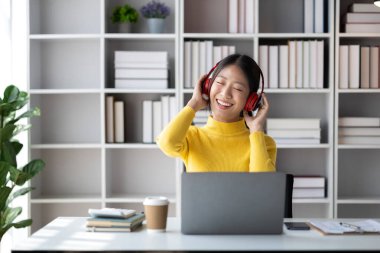 Asyalı genç bir kadın dizüstü bilgisayarla beyaz ofiste oturuyor, evde bilgisayarla internetten öğrenim görüyor, online internet eğitimi alıyor, internet üzerinden eğitim görüyor..