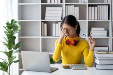 Beyaz odada dizüstü bilgisayarla oturan genç bir kadın, stresli, evde dizüstü bilgisayarla çalışan bir öğrenci, online olarak okuyan bir üniversite öğrencisi, online web eğitimi kavramı.