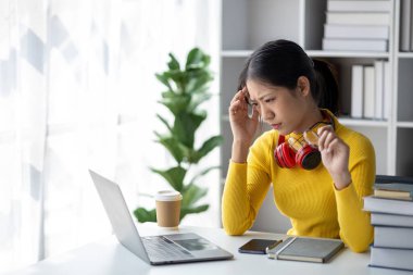 Beyaz odada dizüstü bilgisayarla oturan genç bir kadın, stresli, evde dizüstü bilgisayarla çalışan bir öğrenci, online olarak okuyan bir üniversite öğrencisi, online web eğitimi kavramı.