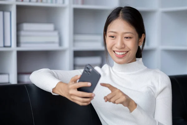 Beautiful Asian woman playing mobile phone in her break from work, she is a marketing manager of a startup company, female leader, supervisor, ceo. Female Leadership Concept.