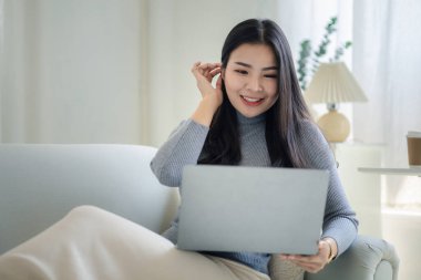 Woman plays on laptop on the sofa in her living room at home, she is resting on weekends after a hard day's work, she relaxes by watching movies and listening to music on her tablet. Holiday concept.