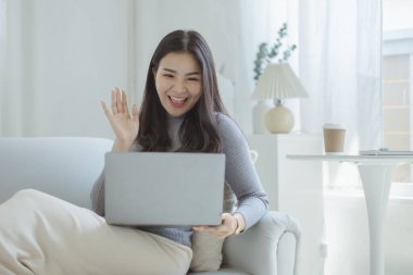 Woman plays on laptop on the sofa in her living room at home, she is resting on weekends after a hard day's work, she relaxes by watching movies and listening to music on her tablet. Holiday concept.