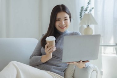 Woman plays on laptop on the sofa in her living room at home, she is resting on weekends after a hard day's work, she relaxes by watching movies and listening to music on her tablet. Holiday concept.