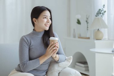 Elinde kahve fincanı tutan bir kadın. O, tatilde oturma odasındaki kanepede dinleniyor. Yoga pozları verip yorucu bir iş gününden sonra rahatlıyor. Sıkı çalışmaya ara verme fikri..