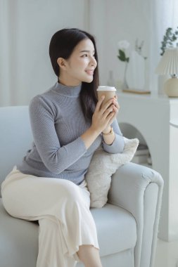 Elinde kahve fincanı tutan bir kadın. O, tatilde oturma odasındaki kanepede dinleniyor. Yoga pozları verip yorucu bir iş gününden sonra rahatlıyor. Sıkı çalışmaya ara verme fikri..