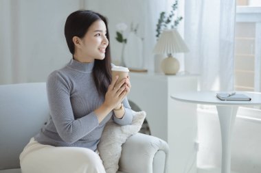 Elinde kahve fincanı tutan bir kadın. O, tatilde oturma odasındaki kanepede dinleniyor. Yoga pozları verip yorucu bir iş gününden sonra rahatlıyor. Sıkı çalışmaya ara verme fikri..