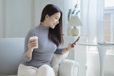 Oturma odasındaki kanepede akıllı telefon oynayan bir kadın, yoğun bir iş gününden sonra hafta sonları dinleniyor, internetten alışveriş yapıyor ve kredi kartıyla ödüyor. Kredi kartı ödeme kavramı.