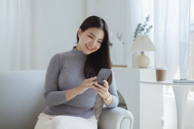 Oturma odasındaki kanepede akıllı telefon oynayan bir kadın, yoğun bir iş gününden sonra hafta sonları dinleniyor, internetten alışveriş yapıyor ve kredi kartıyla ödüyor. Kredi kartı ödeme kavramı.