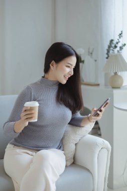 Oturma odasındaki kanepede akıllı telefon oynayan bir kadın, yoğun bir iş gününden sonra hafta sonları dinleniyor, internetten alışveriş yapıyor ve kredi kartıyla ödüyor. Kredi kartı ödeme kavramı.