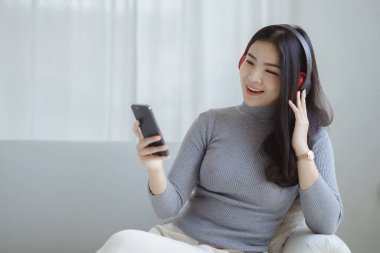 Asyalı bir kadın evinde kanepede dizüstü bilgisayardan müzik eşliğinde dans ediyor, hafta sonu molası, sıkı çalışmaktan dinlenme, kahve içme. Yorucu bir günün ardından tatile çık..