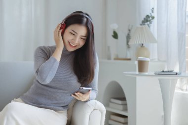 Asyalı bir kadın evinde kanepede dizüstü bilgisayardan müzik eşliğinde dans ediyor, hafta sonu molası, sıkı çalışmaktan dinlenme, kahve içme. Yorucu bir günün ardından tatile çık..