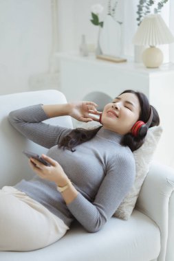 Asyalı bir kadın evinde kanepede dizüstü bilgisayardan müzik eşliğinde dans ediyor, hafta sonu molası, sıkı çalışmaktan dinlenme, kahve içme. Yorucu bir günün ardından tatile çık..