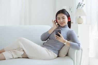 Asyalı bir kadın evinde kanepede dizüstü bilgisayardan müzik eşliğinde dans ediyor, hafta sonu molası, sıkı çalışmaktan dinlenme, kahve içme. Yorucu bir günün ardından tatile çık..