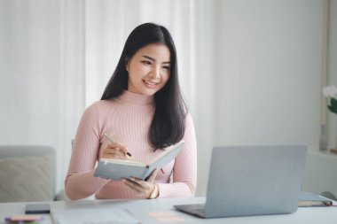 A beautiful Asian businesswoman sitting in her private office, she is checking company financial documents, she is a female executive of a startup company. Concept of financial management.