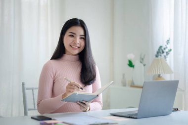 A beautiful Asian businesswoman sitting in her private office, she is checking company financial documents, she is a female executive of a startup company. Concept of financial management.