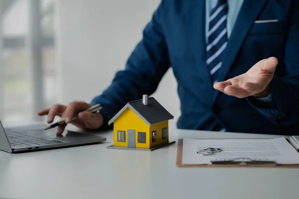 House and real estate agents, house salesmen with house models and house purchase contract documents of housing projects, providing detailed information about real estate. Real estate trading concept.