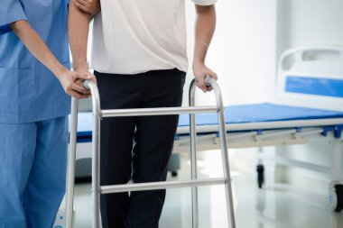 Hasta uzman bir fizyoterapistle fizyoterapi yapıyor, hasta da bir fizyoterapistin yardımıyla yürüyen bir diş teli kullanarak yürüme pratiği yapıyor. Uzmanların fizik tedavi kavramları.