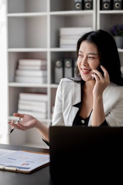 Telefonda konuşan güzel Asyalı kadın, ofiste çalışan iş kadını, şirket kurma işini büyütmek ve modernize etmek için, şirketin pazar ve mali verilerini analiz ediyor..