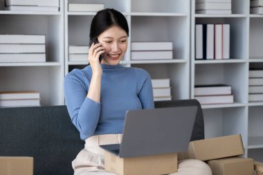 Asyalı kadın çevrimiçi dükkan sahibi, evden çalışan çevrimiçi dükkan sahibi, web sitesinde satılık ürünler yayınlayan ve özel kurye hizmeti sunan müşteriler için siparişleri kabul eden ve paketleyen.