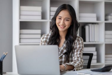 A beautiful Asian businesswoman sitting in her private office, she is checking company financial documents, she is a female executive of a startup company. Concept of financial management.
