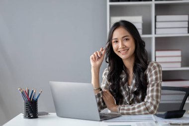 A beautiful Asian businesswoman sitting in her private office, she is checking company financial documents, she is a female executive of a startup company. Concept of financial management.