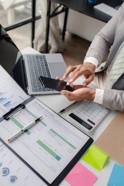 Business man looking at financial information from a mobile phone, he is checking company financial documents, he is an executive of a startup company. Concept of financial management.