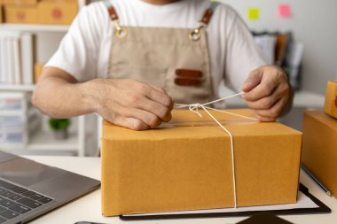 Bir çevrimiçi mağazanın erkek sahibi, ürünleri çevrimiçi satış sitelerinden gelen siparişlere göre paket kutularına koyar, özel kurye hizmeti yoluyla adreslere teslimat için ürünleri paketler. Ürün paketleme kavramı.