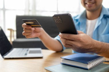 Kredi kartı tutan Asyalı bir adam, İnternet üzerinden mal ve hizmetleri ödemek için kredi dolduruyor ve kredi kartıyla hizmetleri ödüyor. Kredi kartı harcama kavramı.