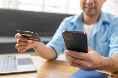 Kredi kartı tutan Asyalı bir adam, İnternet üzerinden mal ve hizmetleri ödemek için kredi dolduruyor ve kredi kartıyla hizmetleri ödüyor. Kredi kartı harcama kavramı.