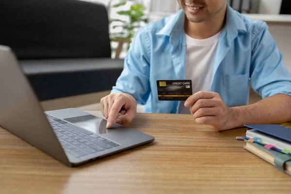 Asian man holding a credit card, he is filling in credit to pay for goods and services on the internet, using credit card to pay for services. Credit card spending concept.