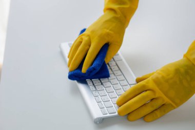 Person cleaning room, cleaning worker is using cloth to wipe computer keyboard in company office room. Cleaning staff. Concept of cleanliness in the organization.