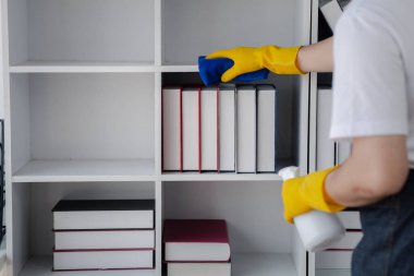 Odayı temizleyen kişi, temizlik personeli şirket ofisindeki kitaplığı silmek için bez ve dezenfektan kullanıyor. Temizlik personeli. Organizasyondaki temizliği sürdürmek.